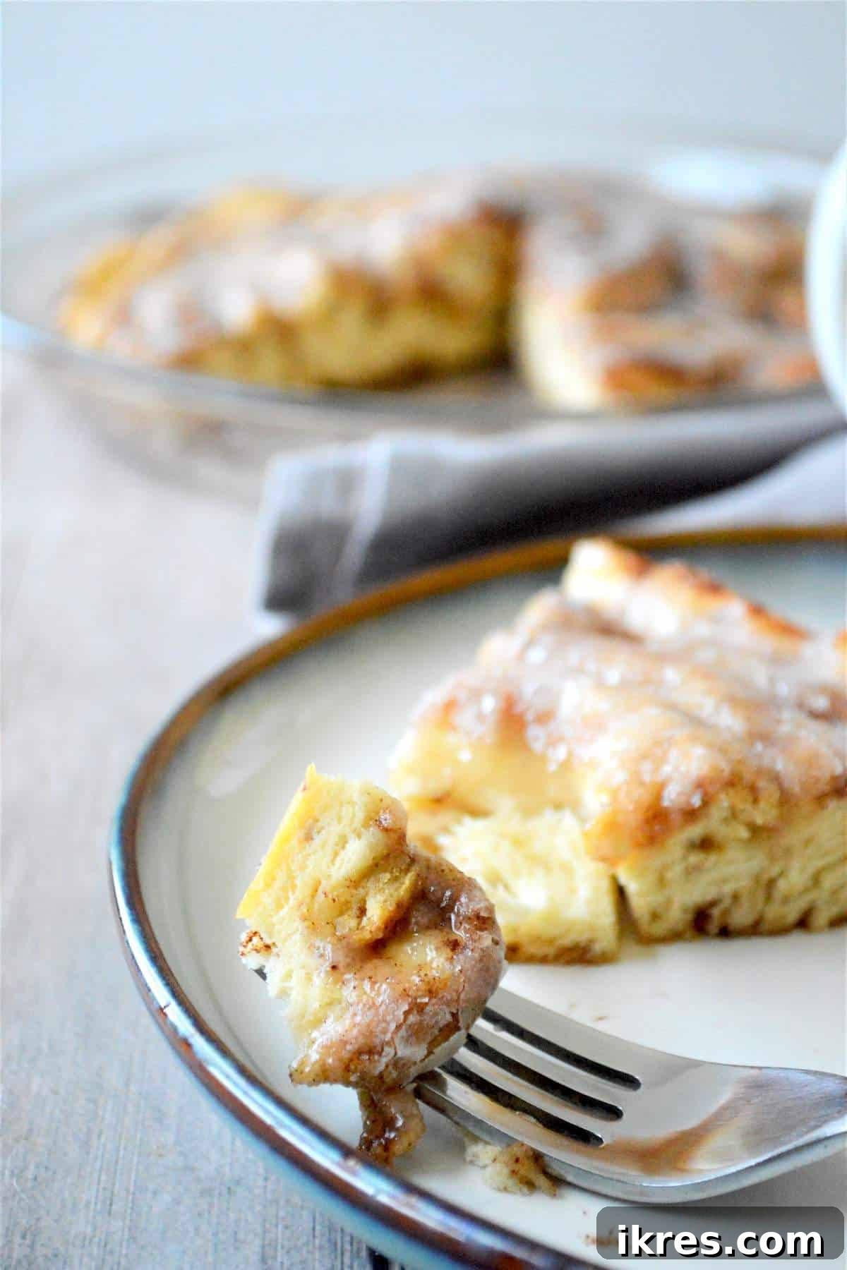A bite of a giant cinnamon roll on a fork next to a full slice on a plate, showing its delicious texture.