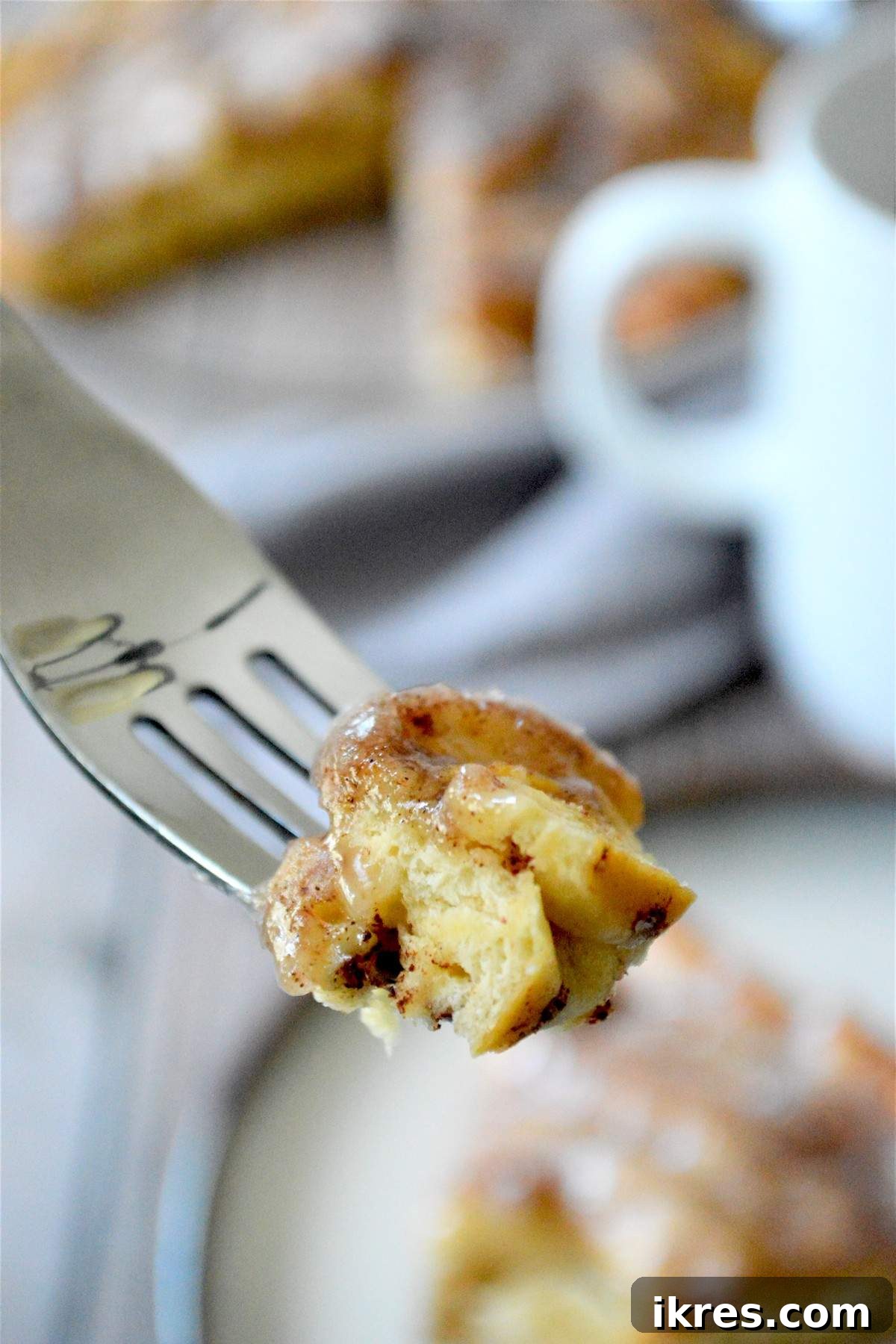 A bite of a giant cinnamon roll on a fork, dripping with cream cheese icing, highlighting its irresistible appeal.
