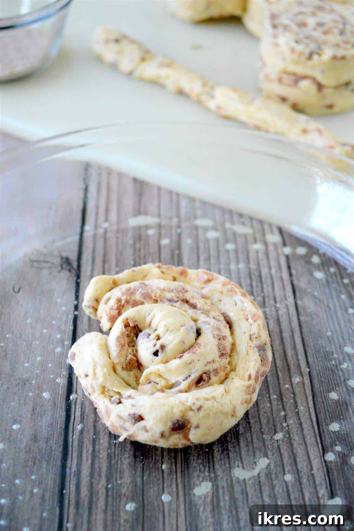 The center of a giant cinnamon roll being formed by spiraling the first strip of unrolled dough in a glass baking dish.