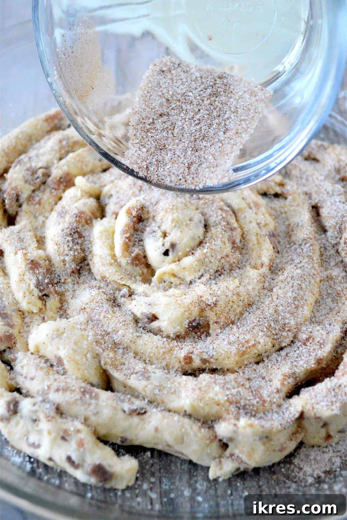 A mixture of cinnamon and sugar being poured evenly over the unbaked giant cinnamon roll.