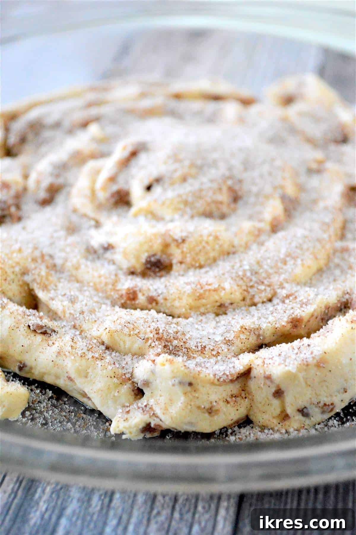 An unbaked giant cinnamon roll in a baking dish, completely covered with cinnamon sugar.