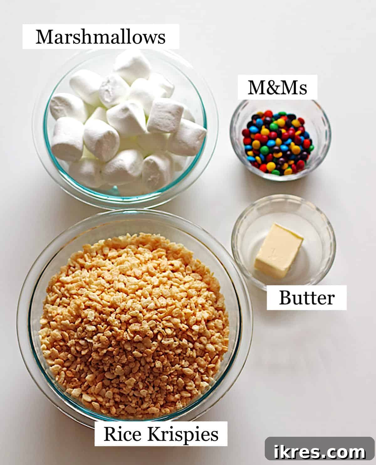 Egg-Cellent Crispy Easter Bites 3 Four clear bowls showcasing the simple ingredients for Rice Krispie Treats: crispy Rice Krispies cereal, fluffy marshmallows, colorful M&M candies, and rich butter.