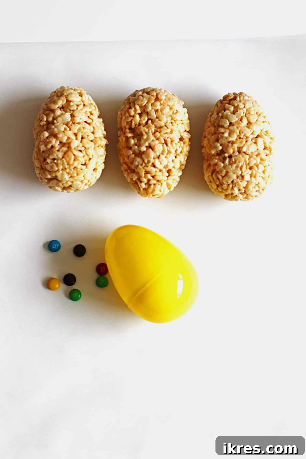 Egg-Cellent Crispy Easter Bites 5 Freshly made Rice Krispie Treat Easter eggs cooling on a counter, with a yellow plastic egg and scattered M&M candies nearby, ready for more creative fun.