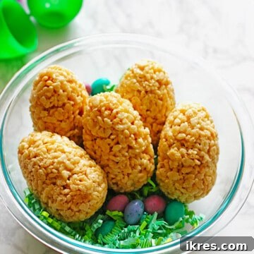 Easter eggs made out of rice krispie treats and filled with M&M's placed in a clear bowl with green easter grass and candy