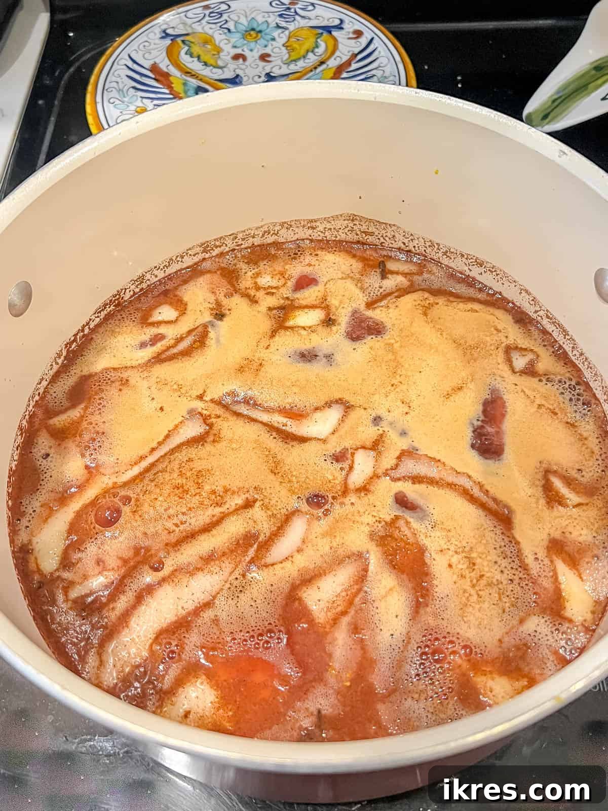 Crimson Pears with Zesty Spice Infusion 9 Spiced poached pears simmering gently in red wine and orange juice on a stovetop, indicating the cooking process.