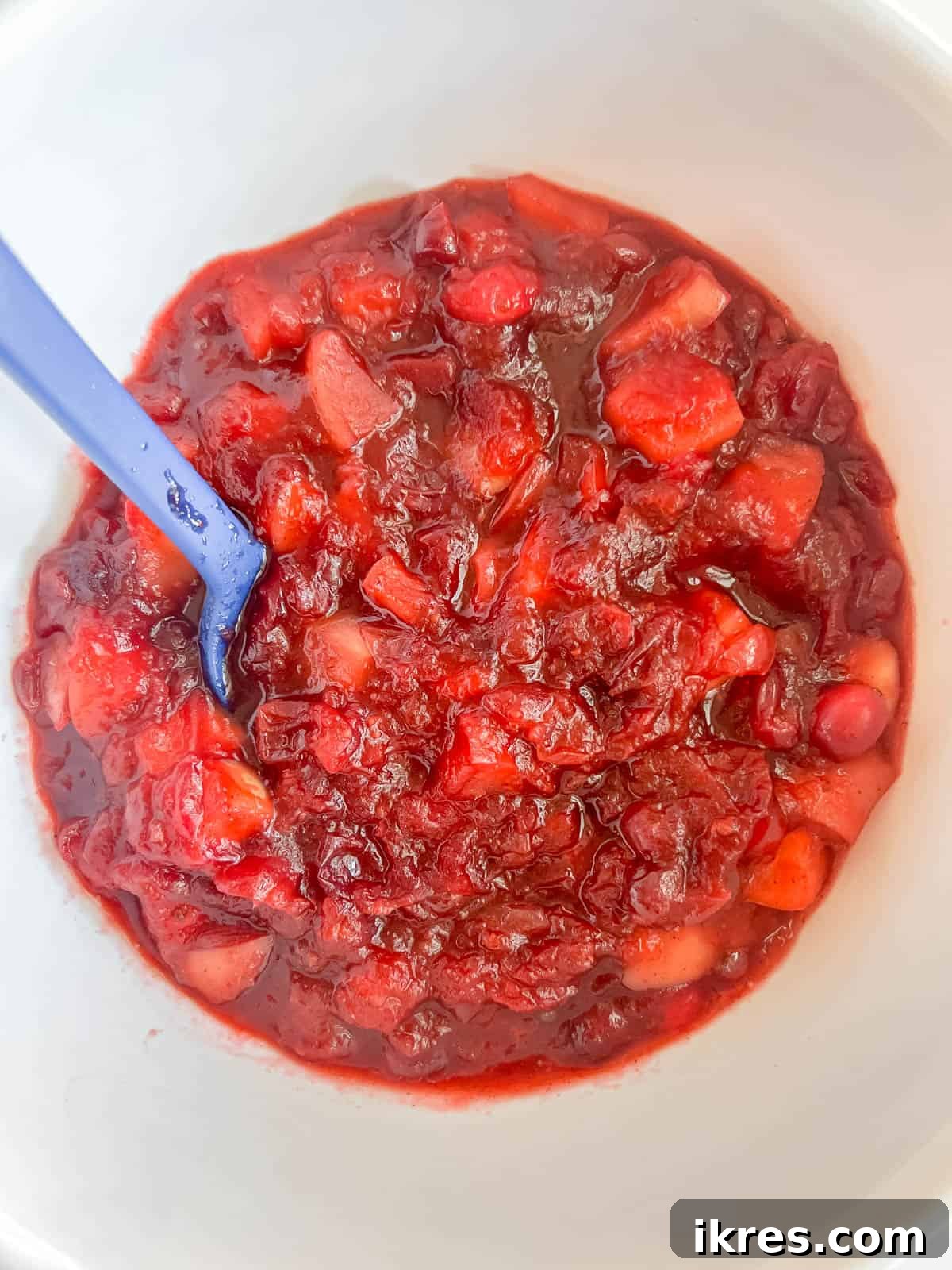 Ruby Apple Cranberry Compote 7 Freshly cooked cranberry apple sauce cooling in a glass bowl, with visible fruit pieces and steam.