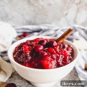 Cranberry apple sauce in a bowl with a cinnamon stick in it.