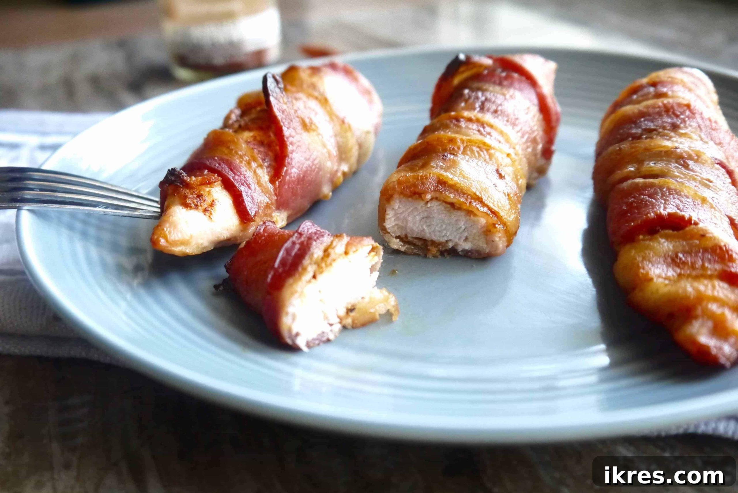 Guilt Free Paleo Keto Bacon Wrapped Chicken Tenders 2 Bacon wrapped chicken tenders on a plate cut into pieces, ready to be enjoyed as a healthy, flavorful meal.