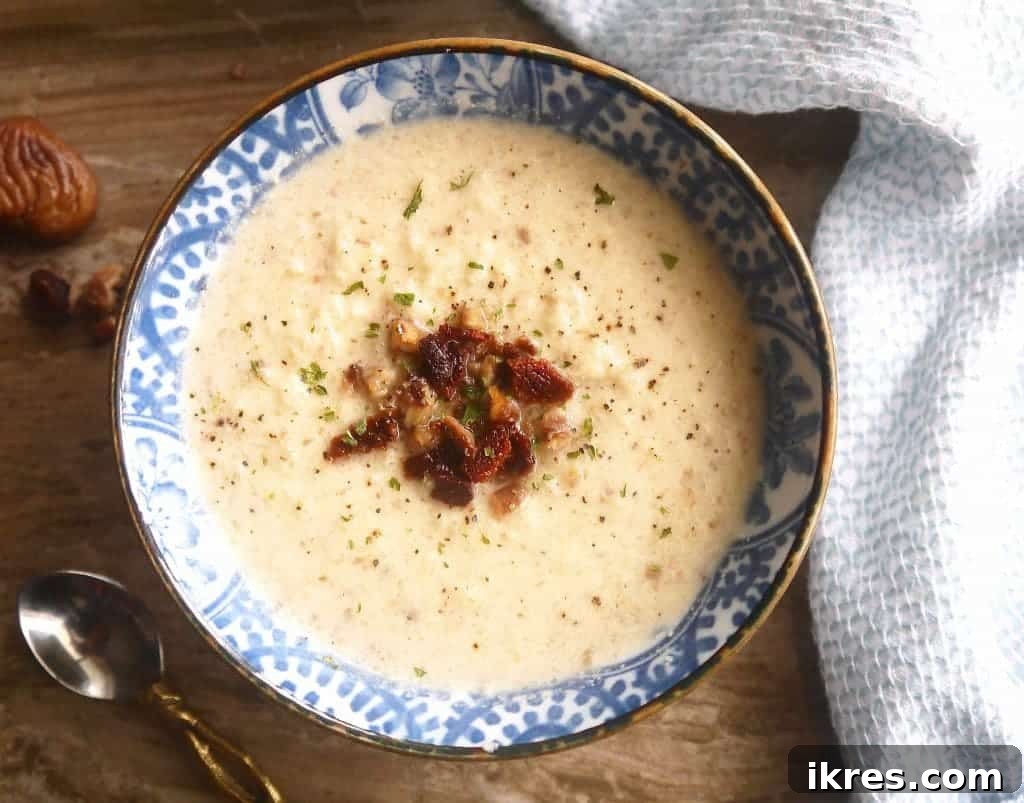 A pot of Paleo Cauliflower, Bacon, and Chestnut Soup simmering on the stove, showing its rich, creamy texture. Healthy winter meal.