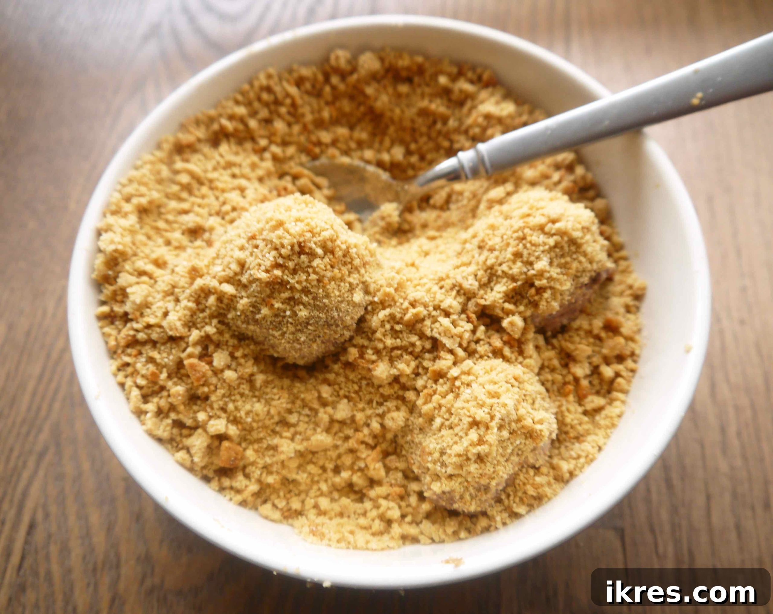 Paleo chocolate mousse ball dropped into a bowl of cookie crumbs and gently covered with a spoon.