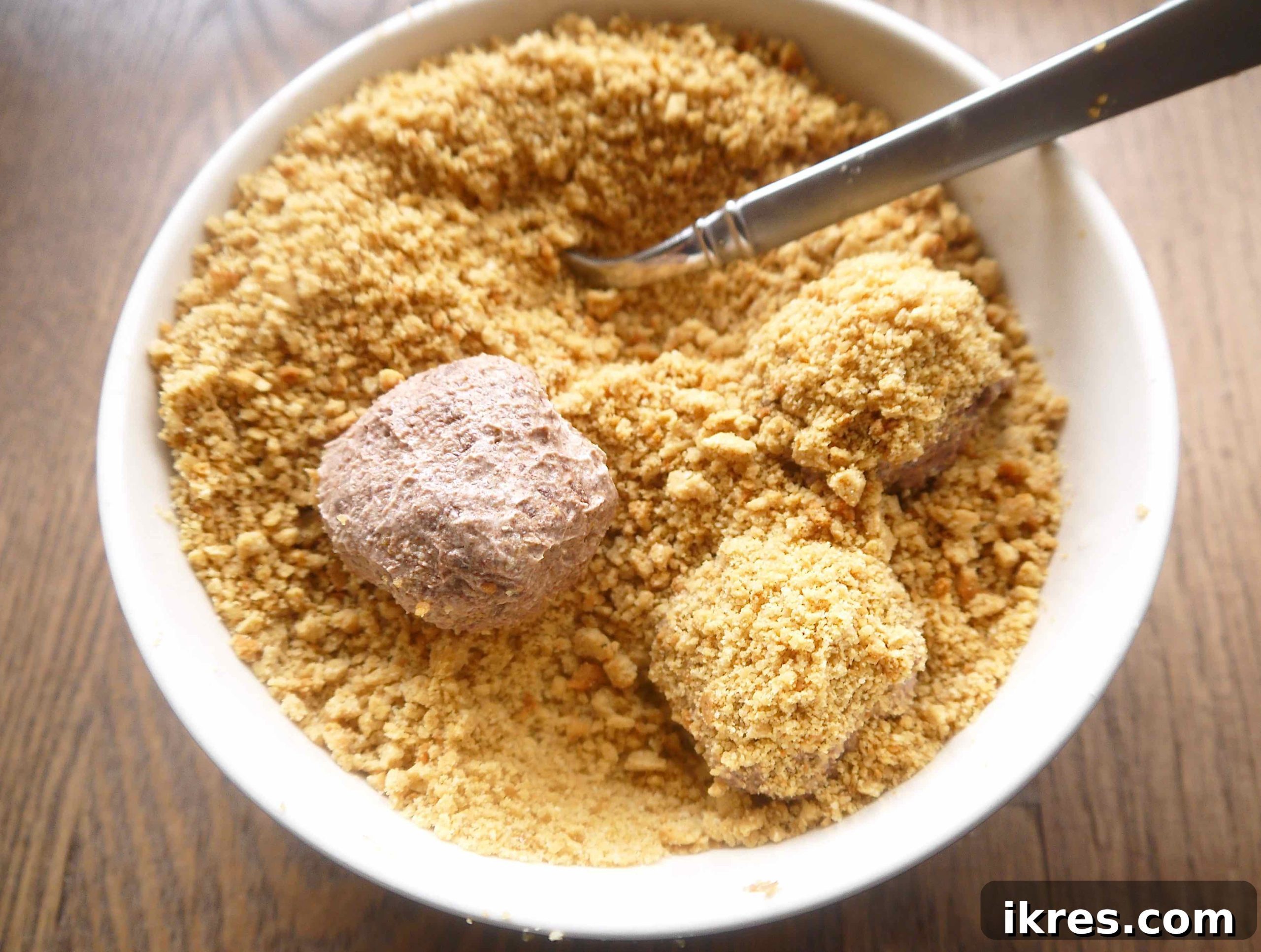 A crumb-covered Paleo chocolate mousse ball being rolled by hand and then returned to the bowl for a second coating of crumbs.