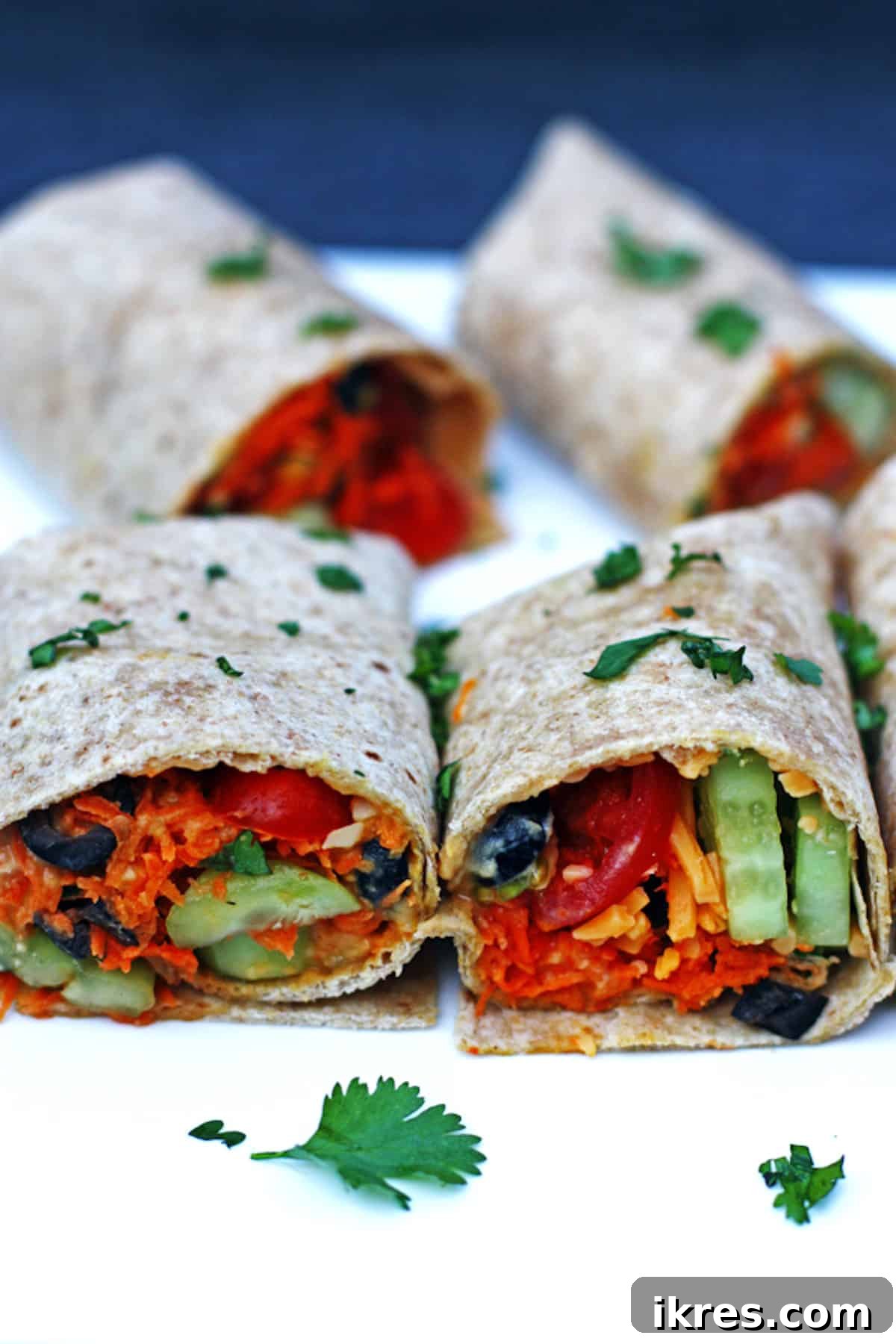 Vibrant Hummus Veggie Wraps 2 Four whole wheat vegetable wraps filled with hummus, crisp carrots, fresh cilantro, sliced olives, and cool cucumber slices, arranged with ripe tomatoes.