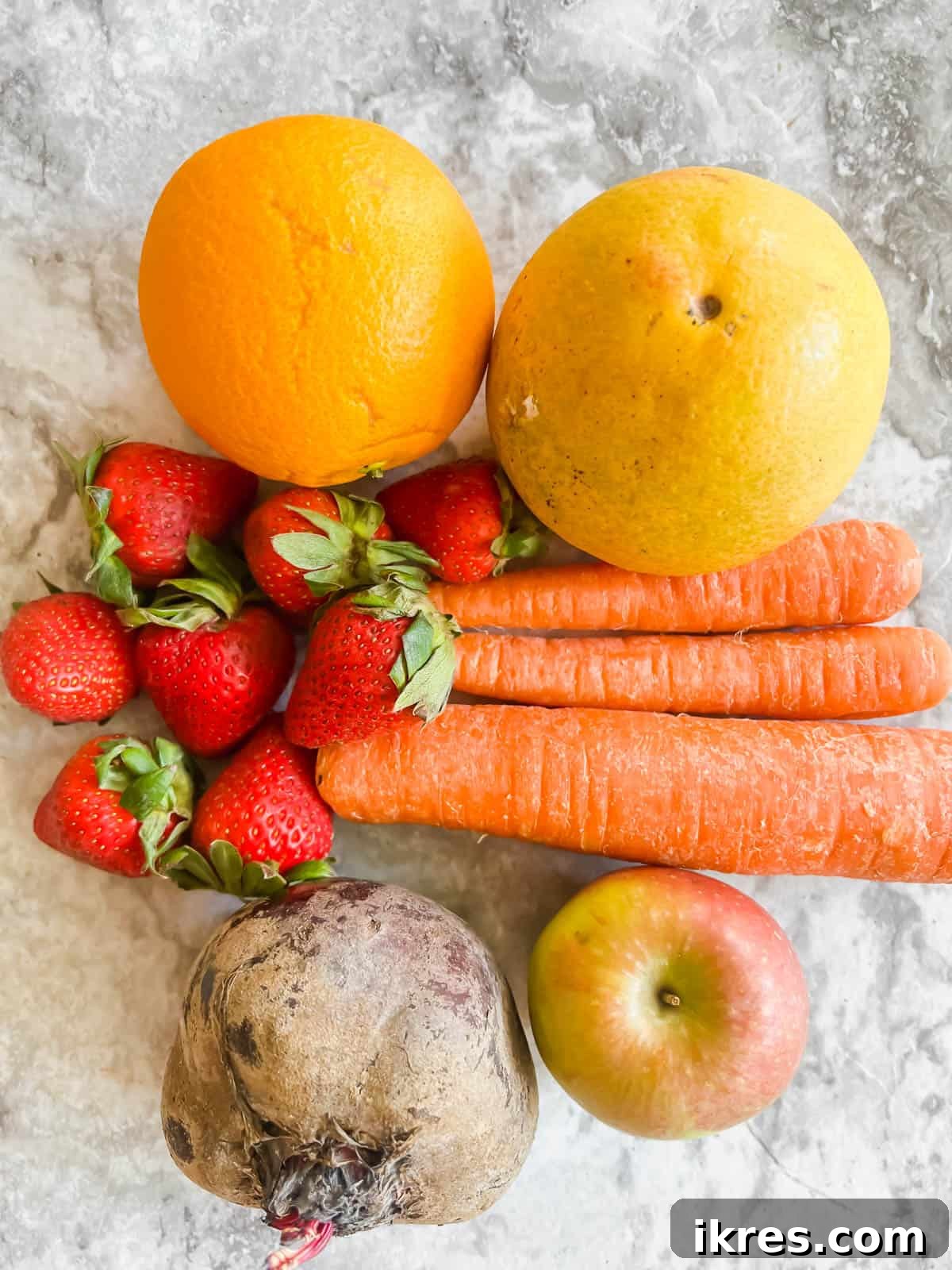 Fresh Ingredients for Strawberry Apple Beet Carrot Juice Recipe A vibrant selection of fresh produce including grapefruits, oranges, carrots, beets, apples, and strawberries laid out on a kitchen counter, ready for juicing.