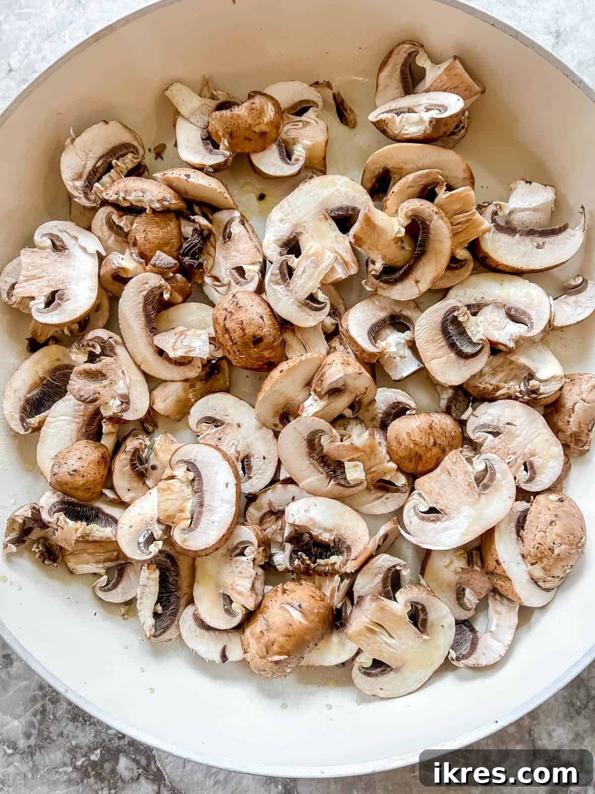 Sliced mushrooms being added to a hot frying pan with olive oil, ready for cooking to create a delicious dairy-free mushroom sauce.