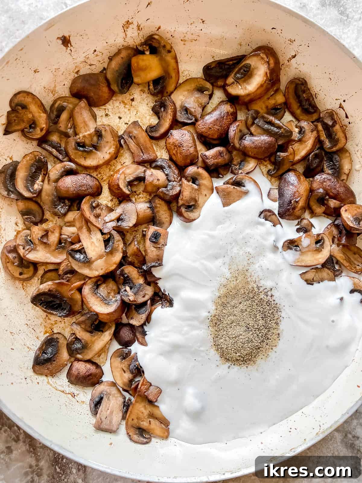 Coconut cream, ground black pepper, and salt are added to the pan with golden-brown cooked mushrooms, ready to be transformed into a creamy dairy-free sauce.