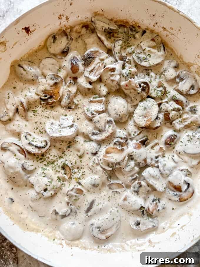 The coconut cream and spices are mixed thoroughly into the mushrooms in the pan, simmering to create a thick and flavorful dairy-free mushroom sauce.