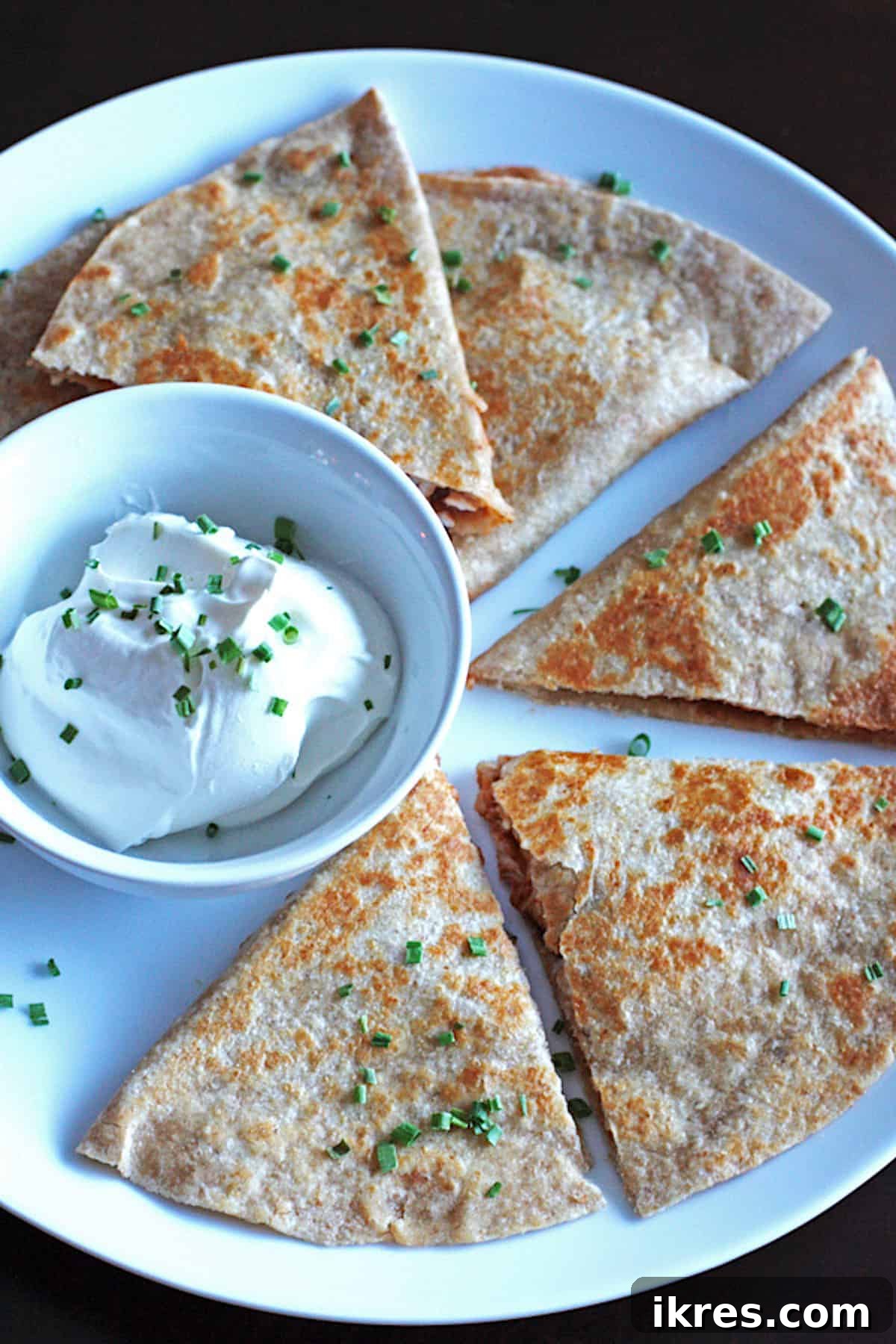Smoky BBQ Chicken Quesadillas 2 Perfectly sliced BBQ chicken quesadillas arranged on a pristine white plate, accompanied by a small bowl of creamy sour cream for dipping.
