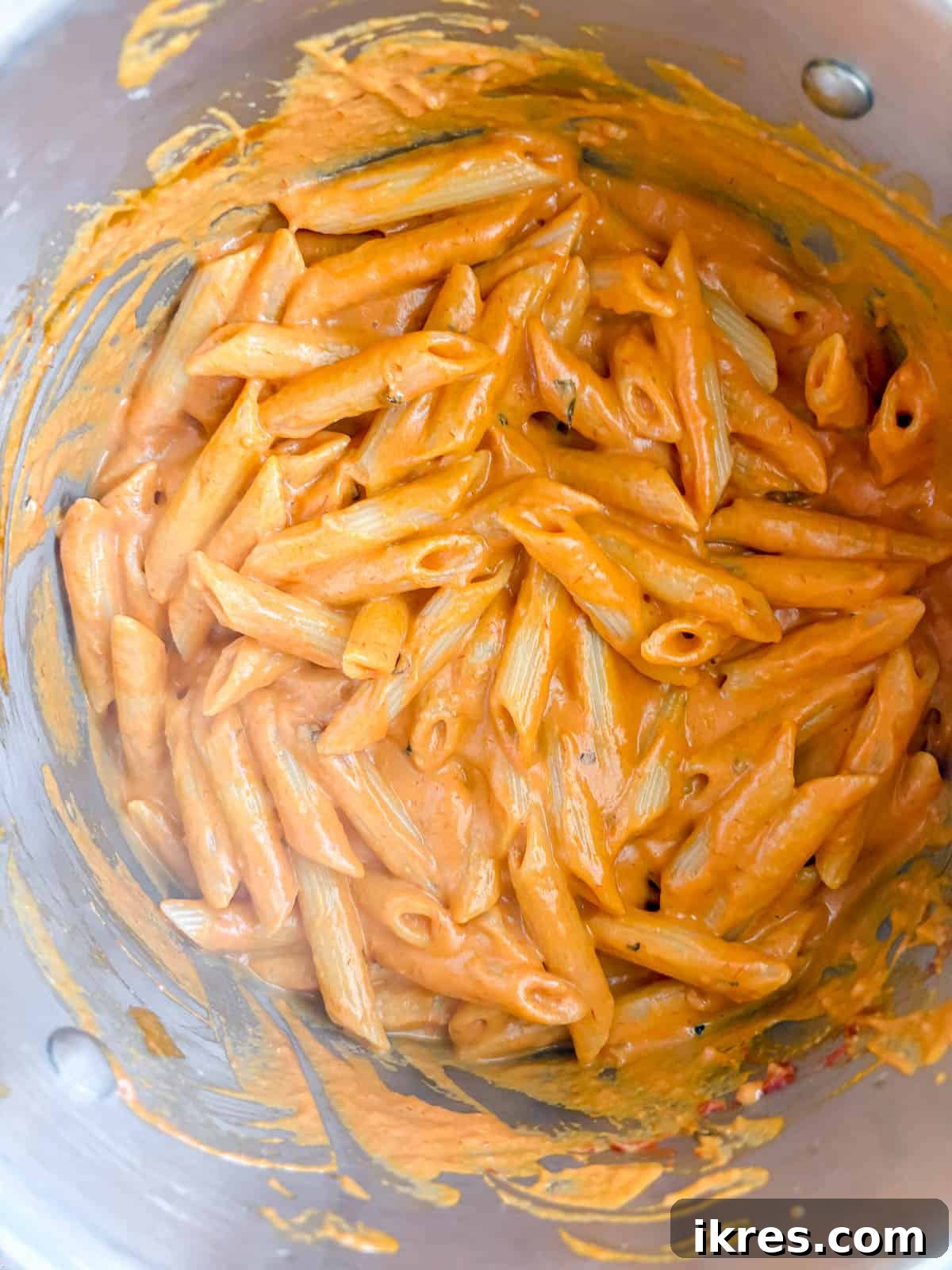 Creamy Vegan Vodka Sauce 8 Cooked penne pasta being tossed into the dairy-free vodka sauce in a pan.