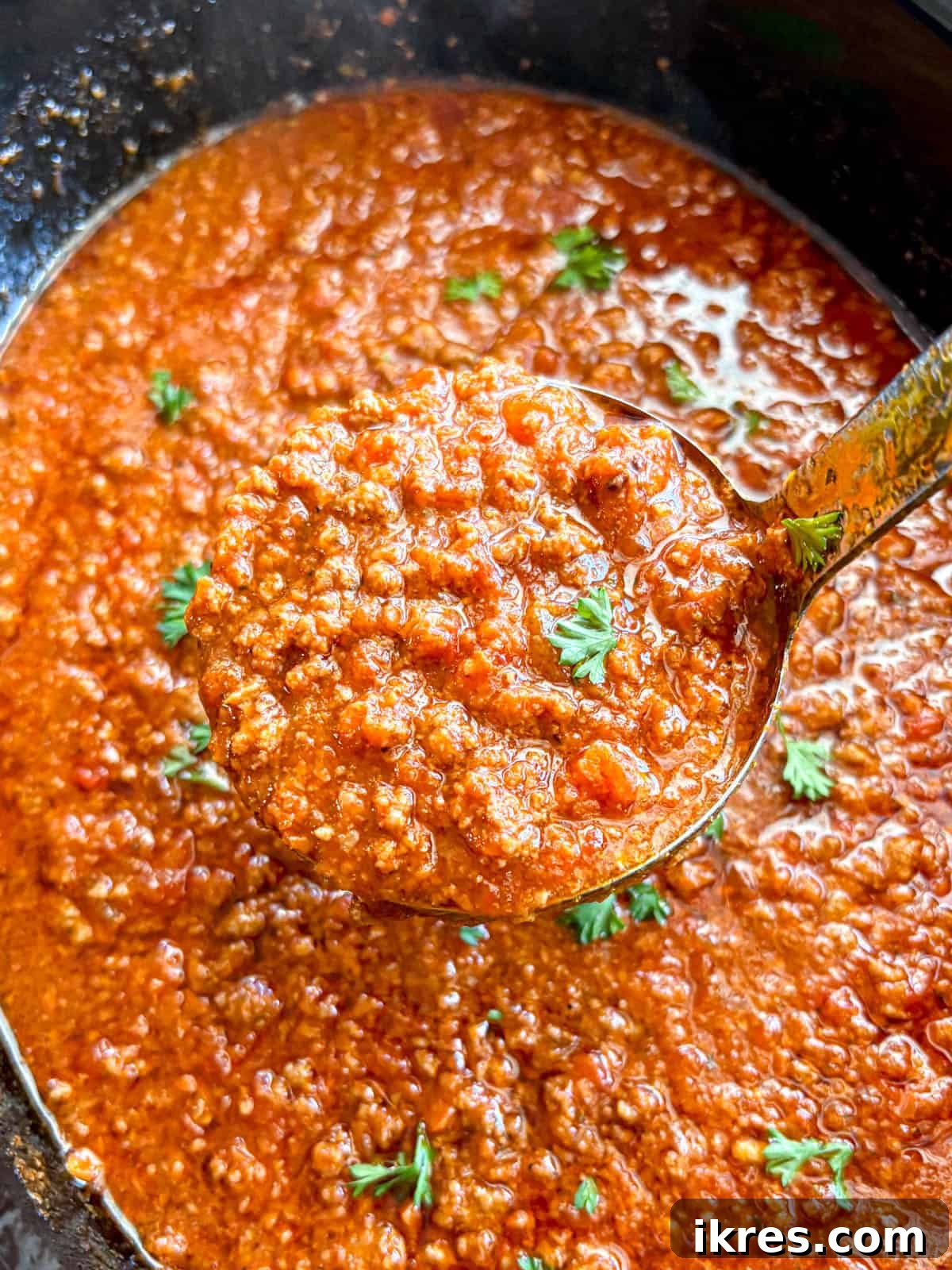 A bubbling slow cooker filled with rich spaghetti sauce with ground beef.