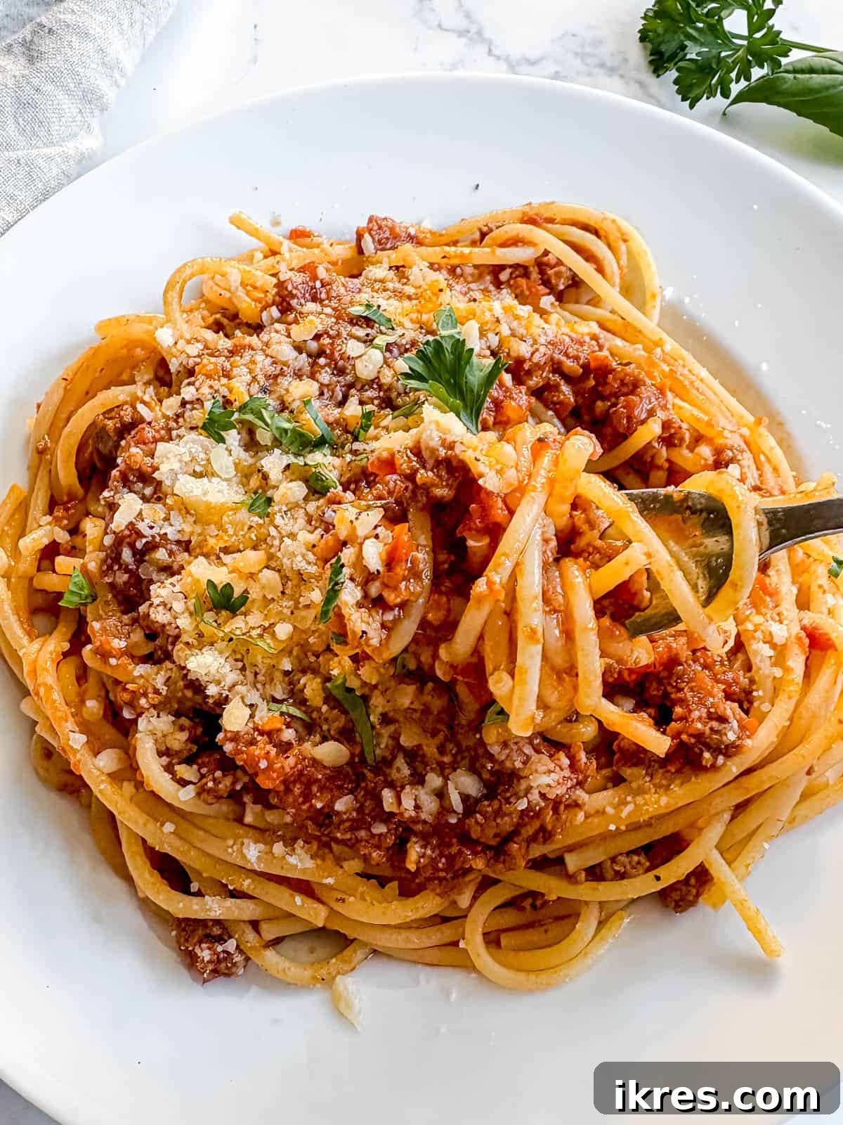 A generous serving of spaghetti covered in slow cooker spaghetti sauce with ground beef, garnished with fresh herbs.