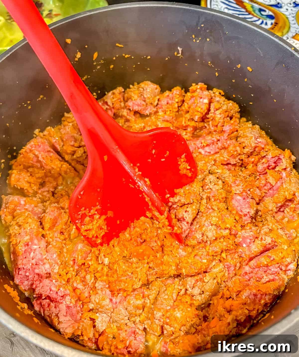 Using a meat masher to break up ground beef in a pan.