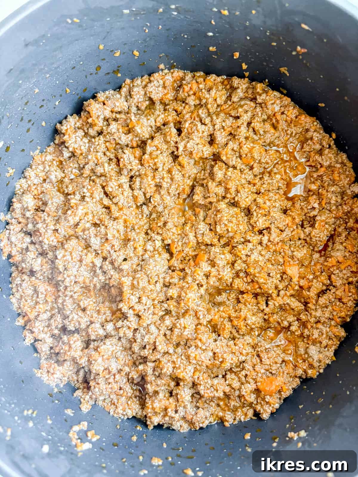 Perfectly browned ground beef mixed with tomato paste in a pan.