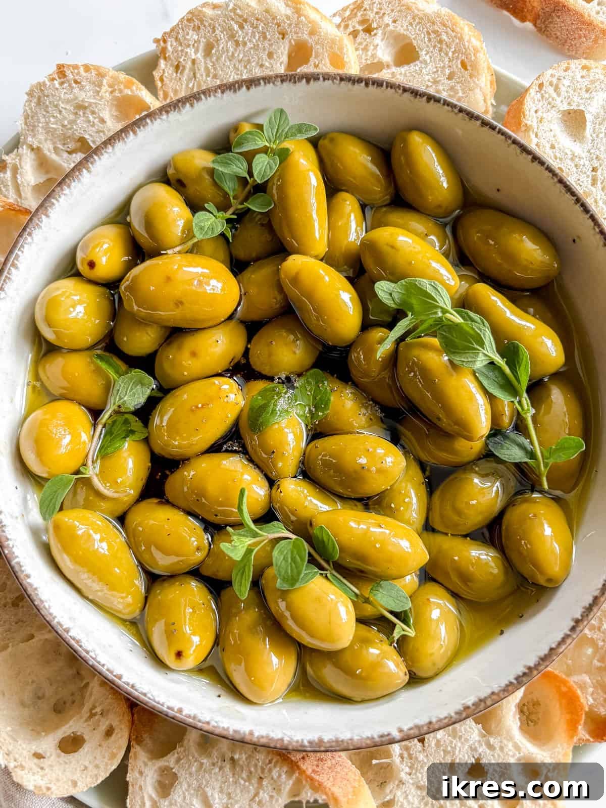 Warm Green Olives Bathed in Balsamic and Olive Oil 5 Warm green olives in a bowl after baking, beautifully garnished with a sprinkle of Maldon sea salt, freshly ground black pepper, and fragrant fresh oregano leaves, enhancing both flavor and presentation.
