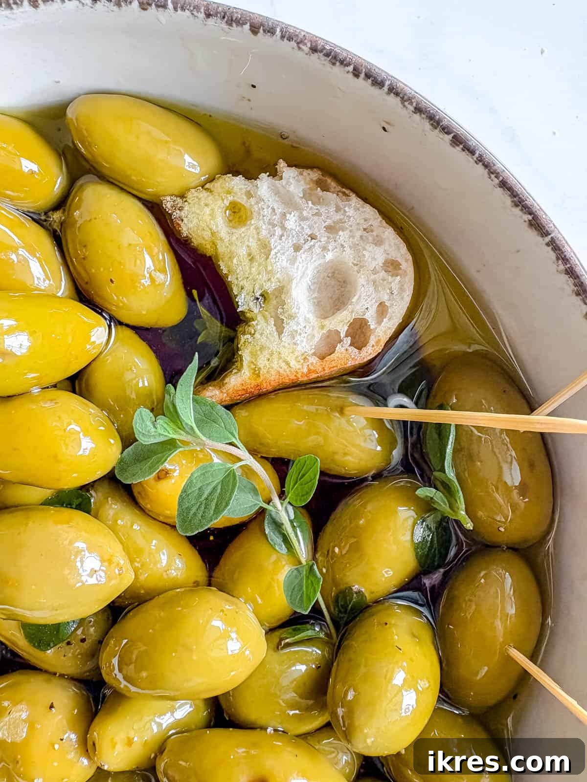 Warm Green Olives Bathed in Balsamic and Olive Oil 6 A slice of crusty toasted baguette being perfectly dipped into the rich, aromatic olive oil and balsamic vinegar mixture that accompanies the warm green olives, highlighting the dish's interactive serving suggestion.