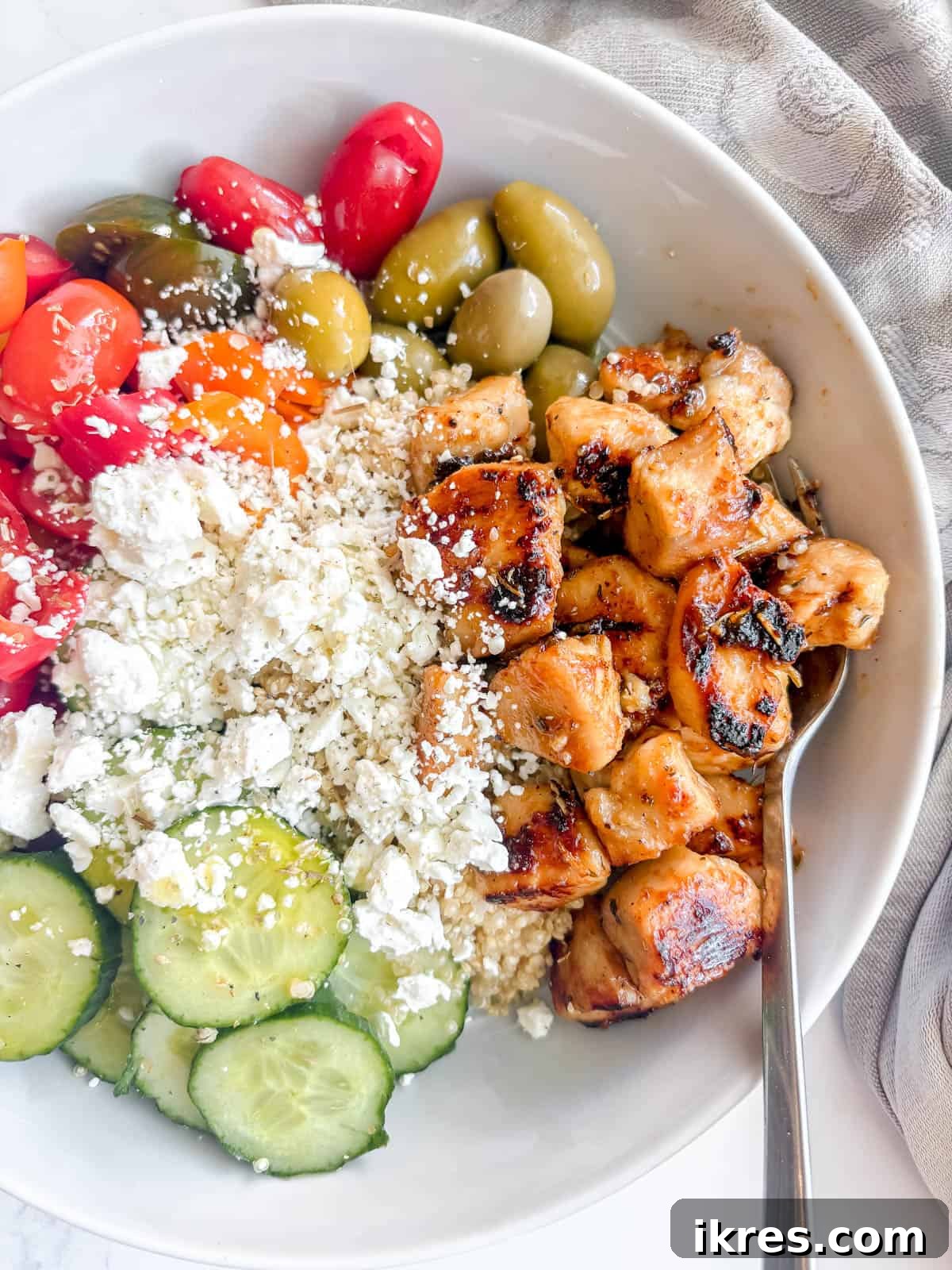 Maple lemon chicken in a bowl with feta, tomatoes, rice, and olives.