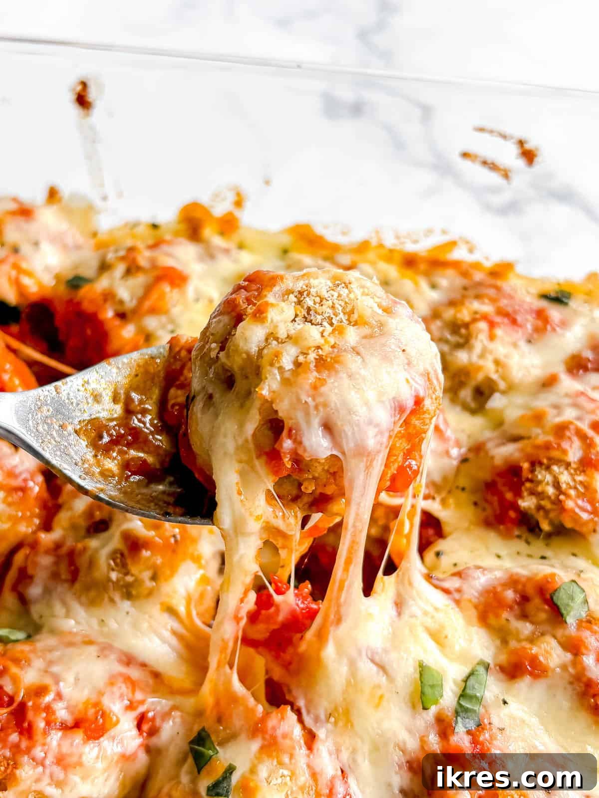 A gooey cheesy chicken parm meatball being lifted out of the dish.
