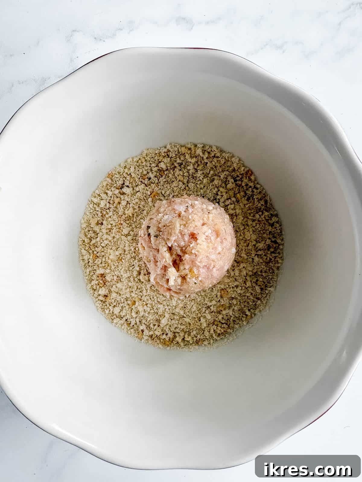 A chicken meatball in a bowl of breadcrumbs. 