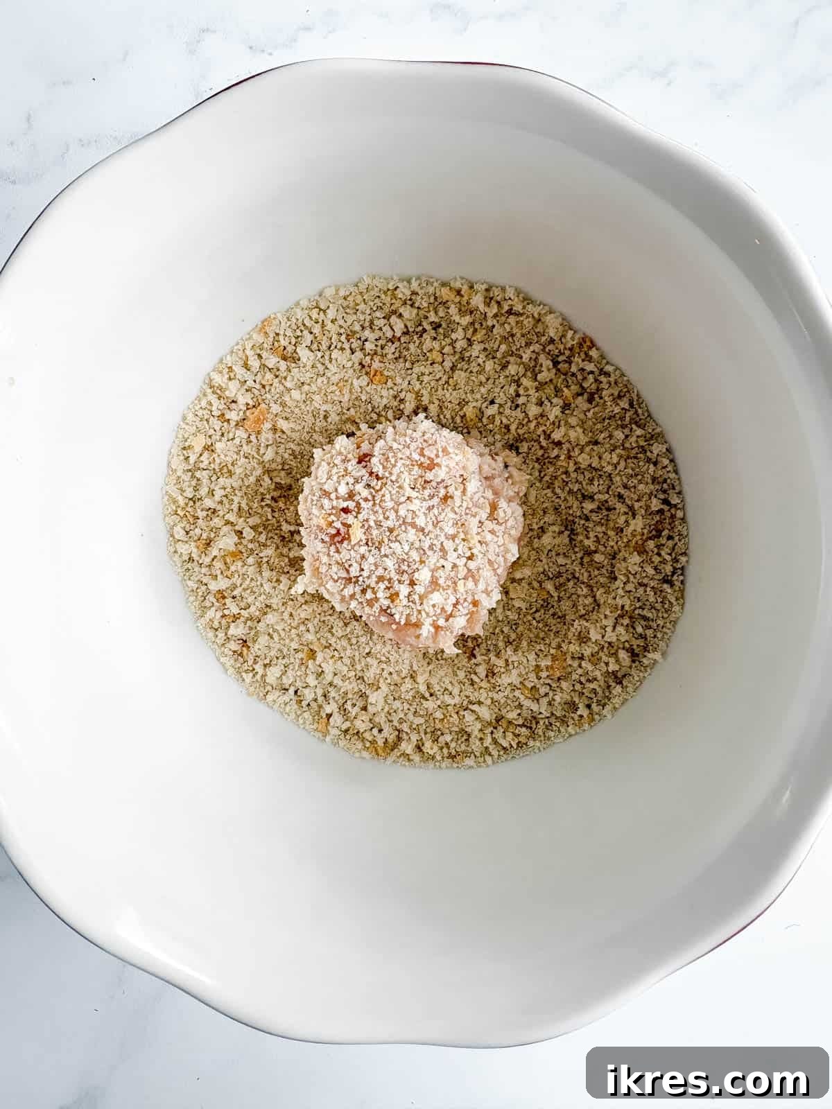 A chicken meatball rolled in a bowl of breadcrumbs. 