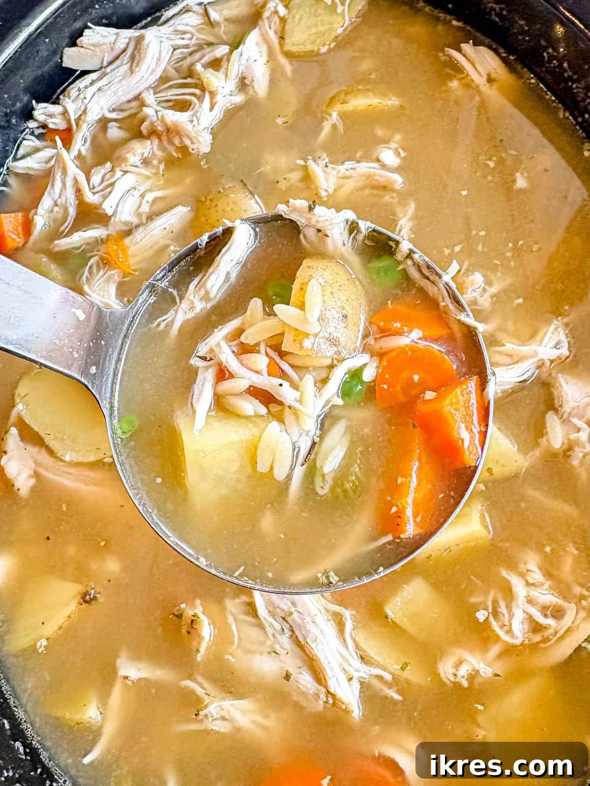 A spoon of crockpot chicken vegetable soup being lifted out of a slow cooker.