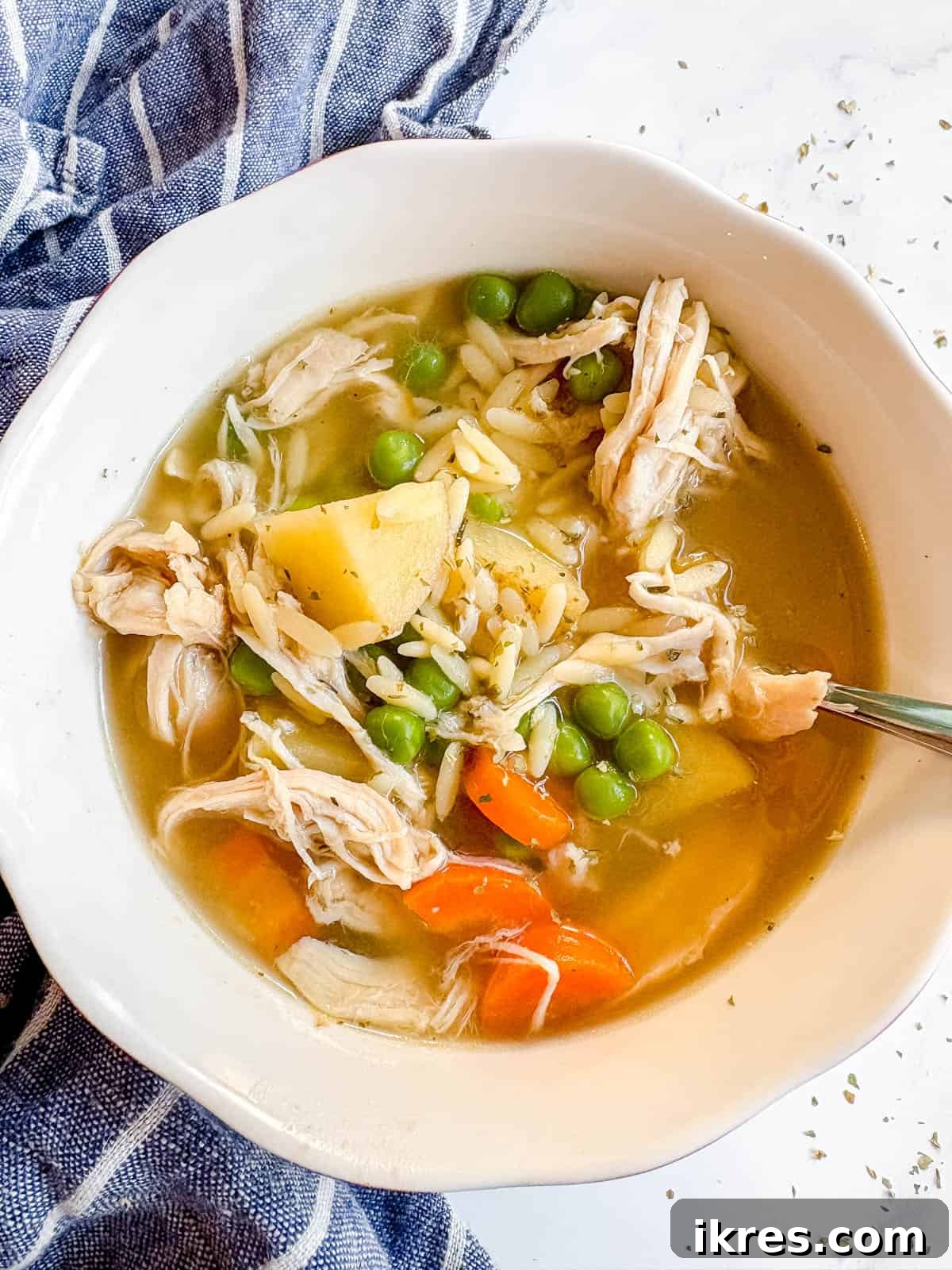 Chicken orzo soup in a bowl with a spoon in it.